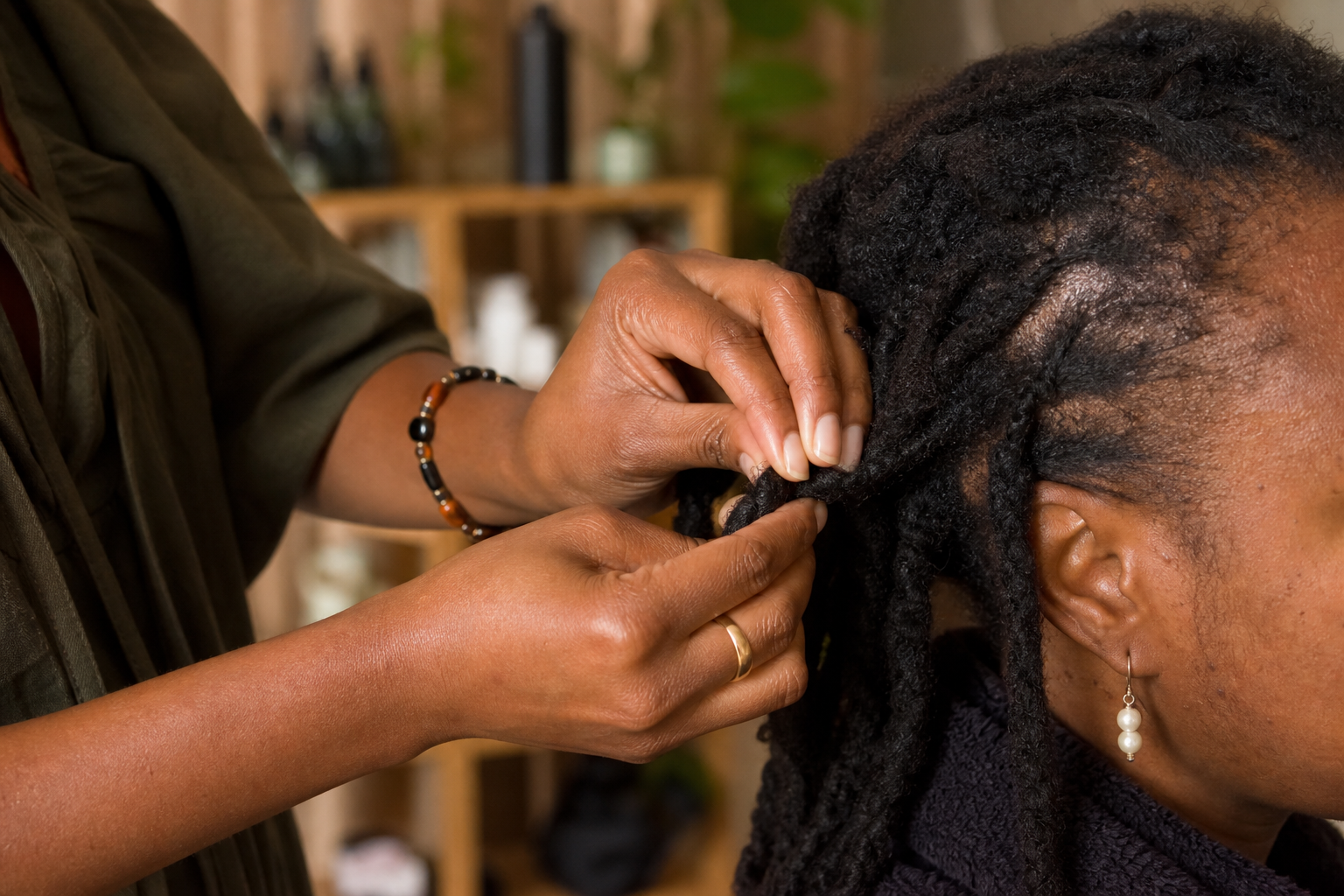 Hands gently working with locs in a warm, intimate salon
